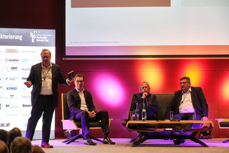 Lars Richter, Frank Schäffler, Markus Exler und Martin Hörmann diskutieren beim 15. Symposium Restrukturierung an der HOK 2026. Richter steht links neben den drei sitzenden Diskussionsteilnehmern.