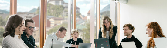 Studierende an der HOK sitzen an einem Tisch mit Laptops und diskutieren in einem hellen Raum mit Blick auf die Festung Kufstein.